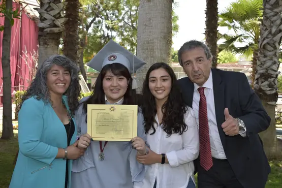 Familiares acompañando a alumna con birrete y toga gris, posterior a la ceremonia