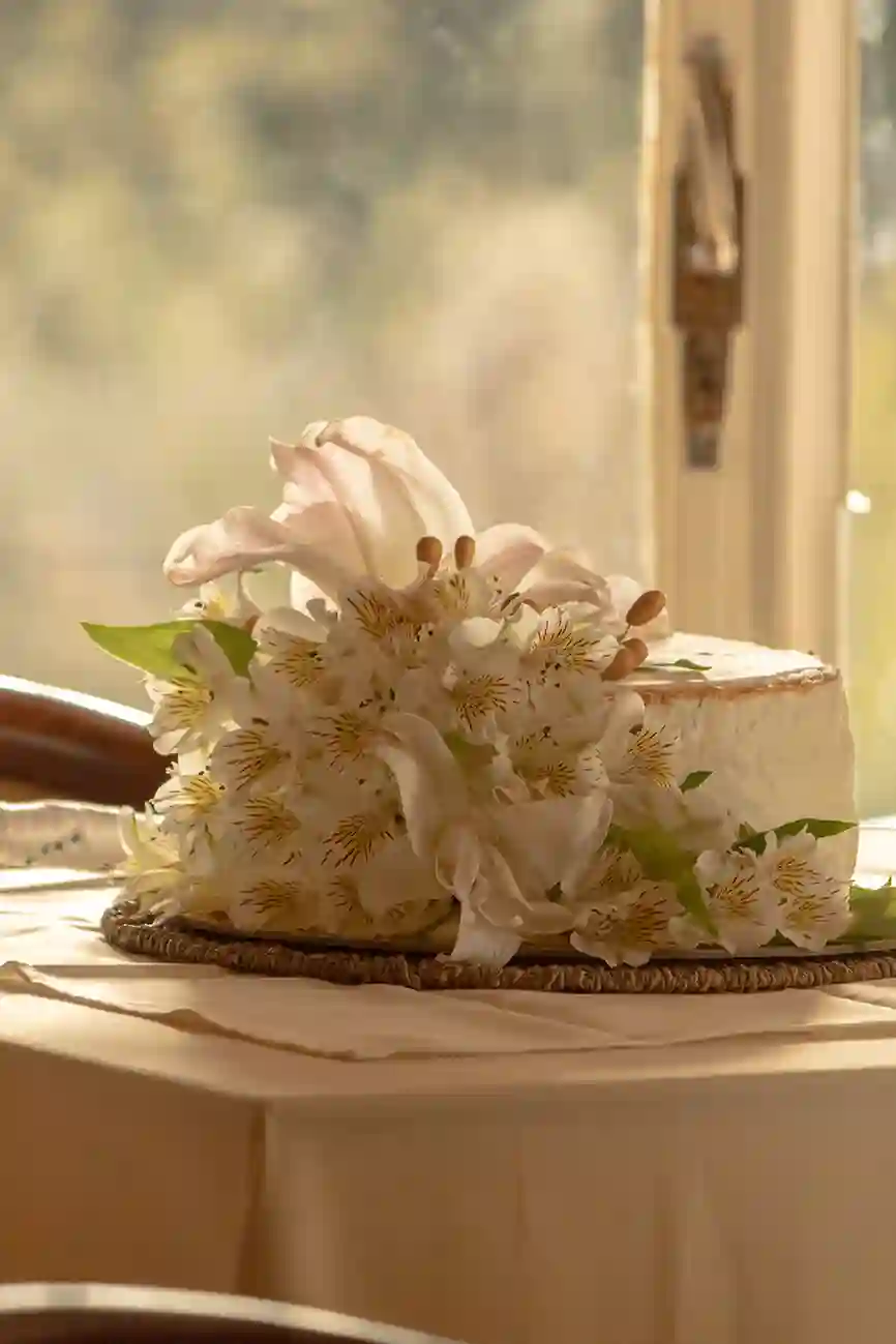 Primer plano a torta de novios de un piso, con muchos adornos, en una mesa, fondo difuminado