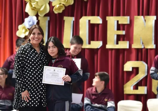 Foto de alumna de octavo básico recibiendo su diploma de graduación junto a su profesora